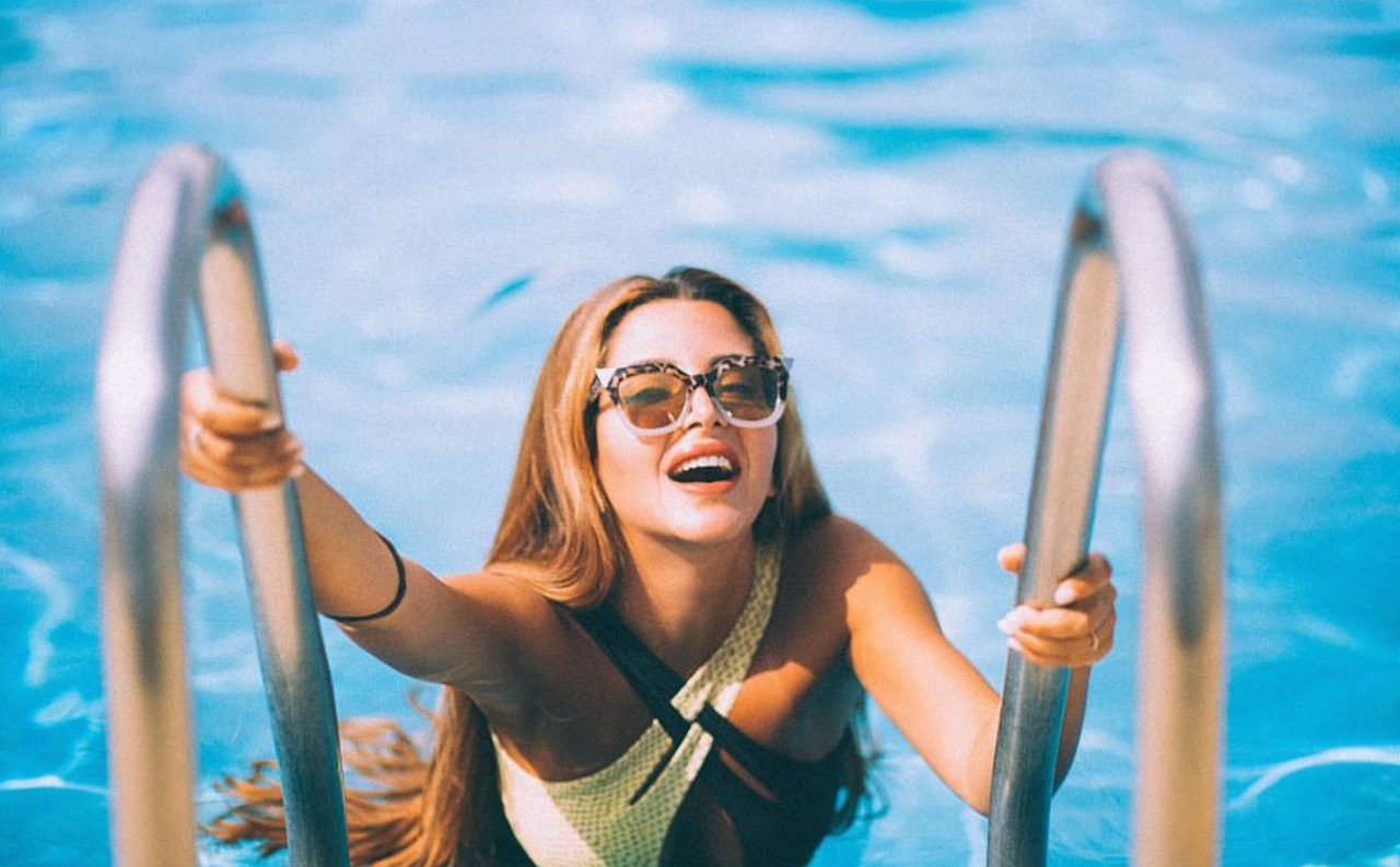Vicentta laughing on a pool ladder in sunglasses
